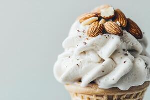 An ice cream cone features a generous swirl of creamy vanilla ice cream, beautifully topped with whole almonds. The simple, light backdrop enhances the desserts enticing appearance. photo