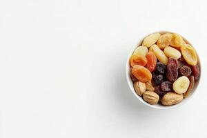 A clean white bowl filled with a colorful assortment of dried fruits and nuts sits on a bright surface. The mix includes raisins, apricots, and almonds, creating a vibrant display. photo