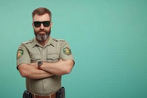 A border control officer poses with arms crossed, exuding authority and vigilance. He wears sunglasses and a uniform, ready to enforce regulations in an official capacity. photo
