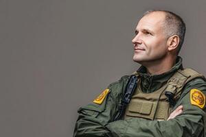 A border control officer is standing with arms crossed, exuding confidence. He wears a uniform featuring a badge, ready to uphold security protocols during his shift at the border. photo