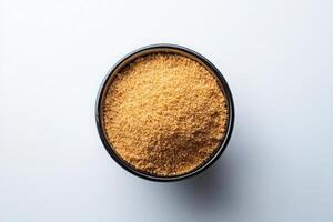 A black bowl filled with finely crushed graham cracker crumbs is prominently displayed on a light surface, showcasing the golden-brown texture and fine consistency of the crumbs. photo