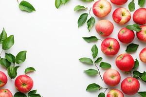 A collection of vibrant red apples surrounded by lush green leaves is arranged artfully on a clean white surface. This setting highlights the freshness and natural beauty of the apples. photo