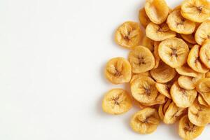 A collection of dried banana chips is beautifully displayed on a pristine white surface, highlighting their golden hue and crunchy texture, making for a healthy snack option. photo