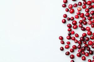 A collection of dried cranberries is scattered on a smooth, clean white surface. Their vibrant red color contrasts beautifully with the background, showcasing their texture and natural allure. photo