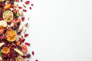 A colorful assortment of dried fruits, including citrus slices, berries, and apple pieces, is artfully arranged on a solid white surface, showcasing its vibrant textures and colors. photo