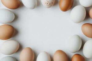 A collection of eggs in different shades of white and brown is arranged in a circular pattern on a light surface. The eggs create an appealing visual display centered in the frame. photo