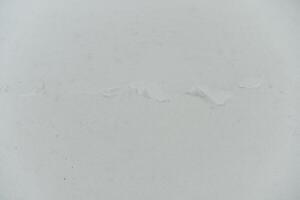 White car body with a small thin scratch or streak of a different color. Scratch is barely visible and appears to be superficial. Rest of the surface is smooth and unmarked. photo