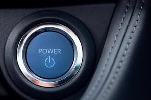 Blue power start engine button with a silver ring surrounding it. The button is illuminated and has a power symbol on it. Button design suggests that it belongs to a modern car model. photo