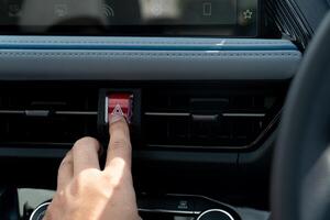 Hand pressing a red button warning emergency light on a car dashboard. The button is likely for an emergency stop or hazard light function. photo