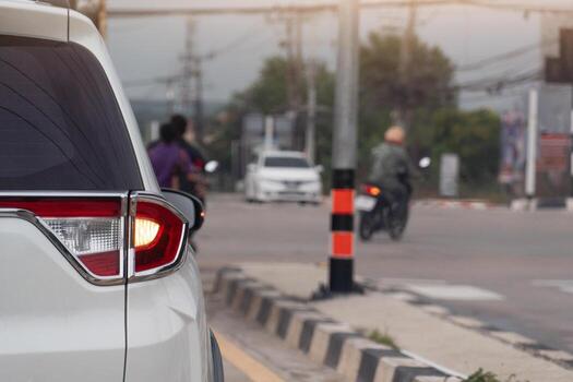 Busy intersection with a white car in the foreground with turn light signal for u-turn. Motorcycle is visible turning right at the intersection. While another vehicle is waiting in the distance. photo