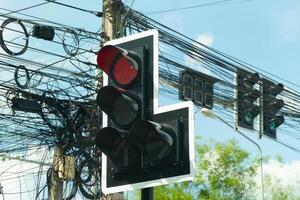 Traffic light with a red light illuminated. Red light indicates that vehicles must stop. Traffic light is surrounded by a network of electrical wires and cables. Under blue sky at day time. photo