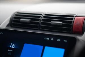 Air conditioning vents and a portion of the dashboard of a car. Red button for emergency case. Dashboard is visible. Including a digital display with a blue background. photo