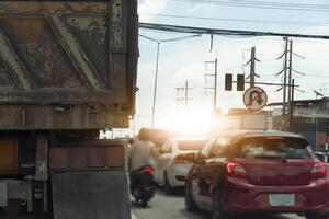 Busy intersection with a variety of vehicles. Including rear side of truck cars and a motorcycle. Sun is setting in the background, casting a warm glow over the scene. photo