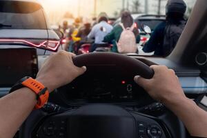 Hand of driver gripping on steering wheel of car. View from the driver perspective shows a traffic jam ahead. with people walking on the sidewalk. Traffic jam on business time. photo