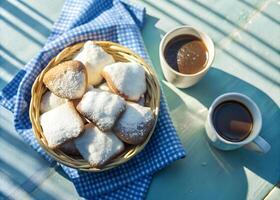Overhead view of a basket of warm beignets, with powdered sugar falling over them, and a cup of chocolate sauce beside it photo