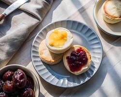 Top view of golden English muffins on a plate, one with butter melting, and the other spread with colorful jam photo