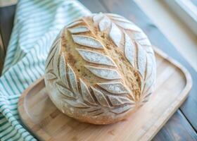 Overhead shot of a whole wheat sourdough loaf on a wooden board, showing the intricate scoring pattern photo
