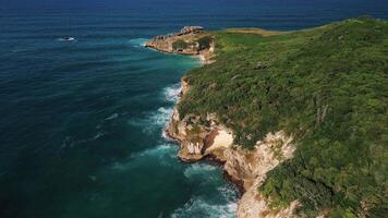 Aerial view of the wild tropical coast of the Dominican Republic with rocky cliff and untouched nature.A light breeze rolls onto shore with turquoise ocean waves.A luxurious landscape for relaxation video