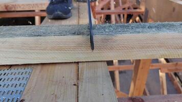 Close-up of a saw blade cutting through a wooden plank during construction with a worker's shoe visible in the background video