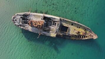 A wrecked wooden ship lies on the seashore, covered with rust. Drone view video