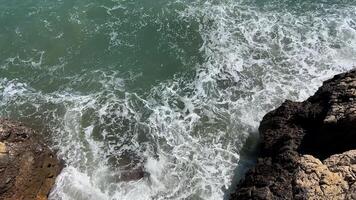 Waves crash against rocky cliffs under sunlight, evoking summer vacations and coastal relaxation video