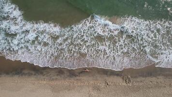 Aerial view of a solitary figure on a sandy beach with crashing waves concepts, relaxation, summer vacation video