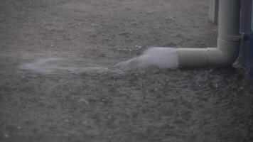 Rain poured down on the cement floor. PVC pipe discharging water onto a concrete surface. The water is creating a spray or mist as it hits the ground. video