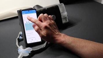 Male European with cpap machine checking therapy analysis via smartphone app or medical app for e health check and health report via mobile device for health analysis innovative sleep apnea mask apps video