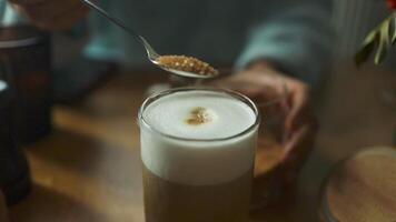 Close-up of male hands pours sugar into coffee. Adding sweetener or fructose to beverage. Hot art Latte Coffee in a cup on wooden table and Coffee shop blur background video