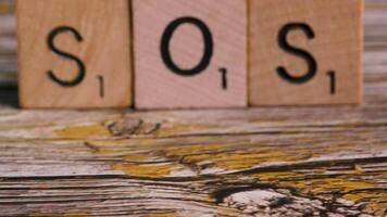 Dolly move on block letters SOS over wood background for urgent message video