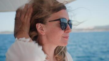 Woman wearing sunglasses enjoys breeze on boat trip with sea in background on sunny day, Summer vacation concept video