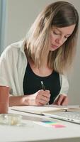 Person is sketching in notebook while working remotely at desk with laptop. Freelance work at home office. Graphic designer drawing sketch video