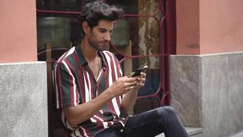 Young man using smart phone sitting on urban step. video