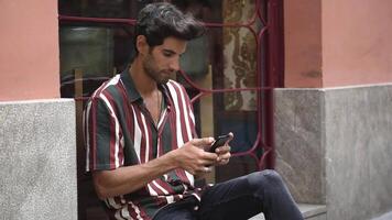 Young man using smart phone sitting on urban step. video