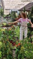 Smiling young female standing and watering plants with hose in green garden video