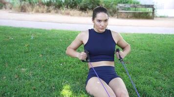 A determined young woman is working out with resistance bands on the grass in an outdoor setting video