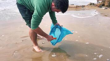 man collects garbage in bag on the seashore, helping environment and cleaning video