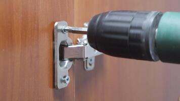 Tighten the screw when installing a door hinge in a wooden cabinet. video
