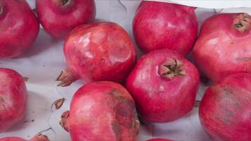 Red ripe pomegranates lie in box on white paper, ready for sale. video