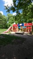 A colorful children's playground with slides and climbing structures in a green park, shaded by trees, beneath a bright blue sky. video