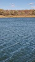 The tranquil river surface reflects a serene autumn landscape with colorful trees along the shore, set beneath a bright, clear sky. video