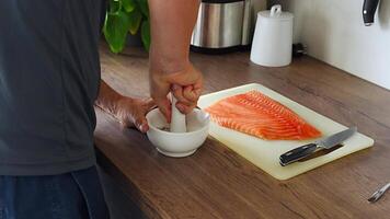 Man grinding spice and dry herbs with a pounder for preparing salmon fish. High quality 4k footage video