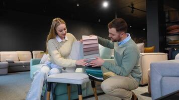 A man and woman choosing upholstery fabric color and texture from various colorful samples for armchair in a store video