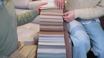 A man and woman choosing upholstery fabric color and texture from various colorful samples for sofa in a store, close up video