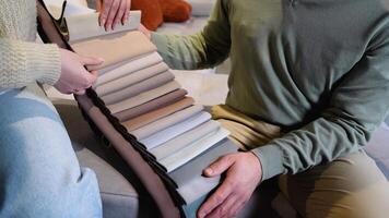 A man and woman choosing upholstery fabric color and texture from various colorful samples for sofa in a store, close up video