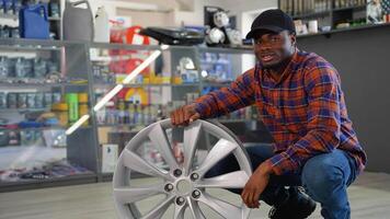 Portrait of a african american seller with a wheel disk in auto parts shop video