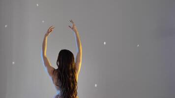 Young woman, ballerina girl dancing, gently moving her hands and fingers on gray background in studio, slow motion, medium shot. A brown-haired lady with long hair from her back, without a face video