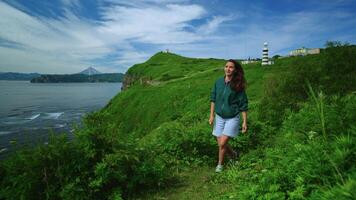 Joyful Brunette Woman Walking Alone On Hills On Oceanic Shore With Lighthouse In Background video