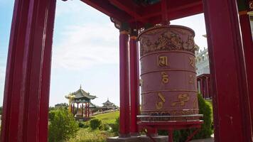 A red Buddhist drum, with mantras inscribed on it, is depicted spinning against a backdrop of a Buddhist temple. video