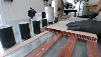 Worker at plant that produces composite materials for furniture manufacturing manually glues side of component on machine. video